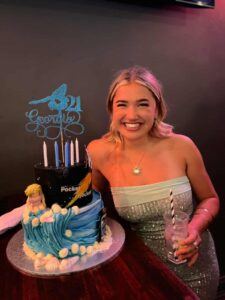 Smiling young woman with a 21st birthday cake decorated with waves, shells and a Kombi van.