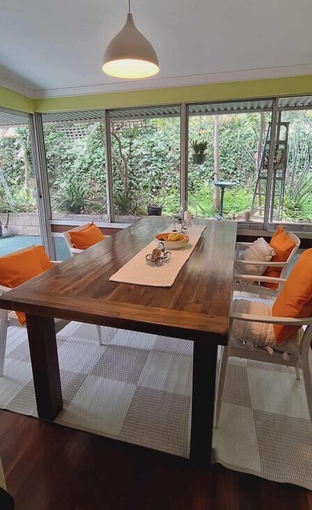 Airy dining room with large wooden table, orange cushions and leafy garden view created with AI design ideas.